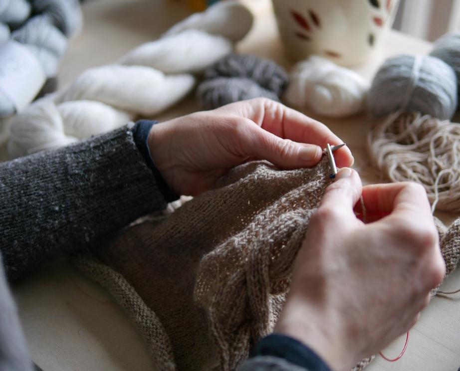 close up of hands knitting surrounded by yarn